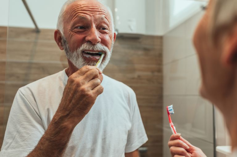 Older man with endodontic treatment smiling and brushing teeth in mirror in Derby