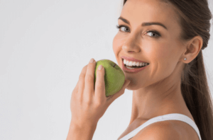 woman eating apple with bright teeth after whitening at duffield health care
